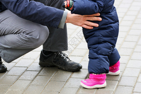 儿童学会走路父亲在孩子旁边蹲着他只是学习走路并赡养它a父母与正在学习走路的孩子同住深蹲男衣服图片