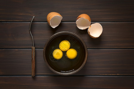 破碎的烘烤新鲜在生锈碗中3个蛋头部镜上面有叉子和折断的蛋壳用天然光照在黑木上图片