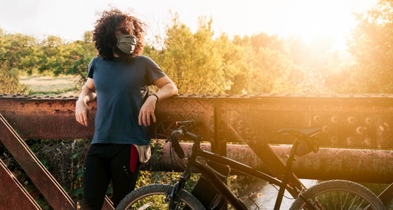 男子在野外佩戴科面罩和骑自行车时在金属桥上用19号鱼群在西班牙的降级时身着脚踏单车年轻的男人自由图片