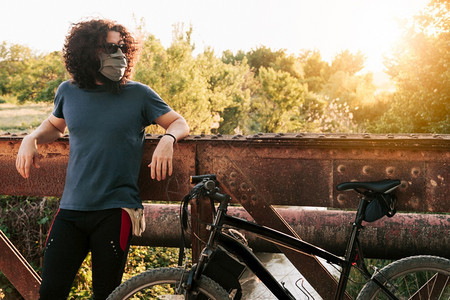 阳光男子在野外佩戴科面罩和骑自行车时在金属桥上用19号鱼群在西班牙的降级时身着脚踏单车疾病户外图片
