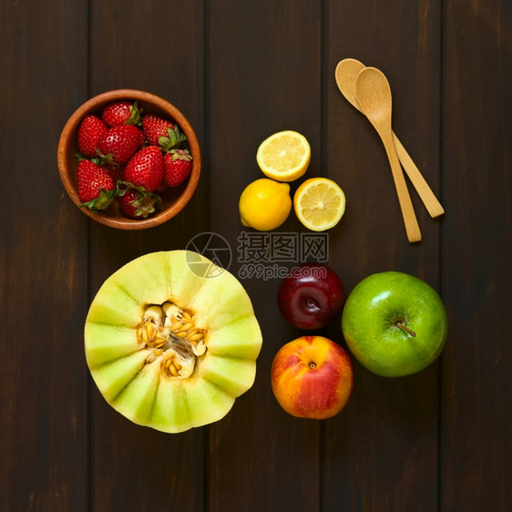 上面拍摄了各种新鲜水果包括蜂蜜甜瓜内橘苹果草莓梅子李柠檬和侧边小木勺子用天然光照在黑木头上新鲜的浆果小吃图片