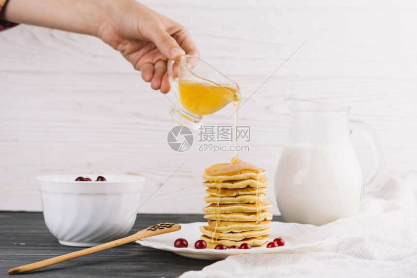 花朵丰富多彩的人手倒蜂蜜美味煎饼木桌的图片