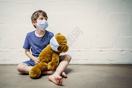 关心坐着安全在共食19年大流行期间带着泰迪熊戴面罩的男孩图片