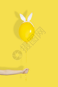 女横幅创意复活节最小概念手拿着一个黄色气球在兔子耳朵单色创意复活节最小概念手拿着一个黄色气球在兔子耳朵单色高架图片