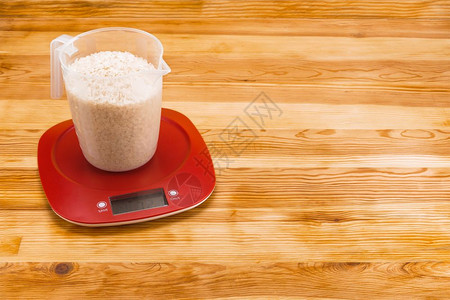电子的蔬菜比率天然木质背景上红色塑料电子秤上透明量杯中的米饭复制空间木质背景上电子秤量杯中的米饭图片