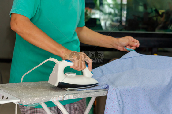 女干净的电妇女手工熨烫蓝色衬衫图片