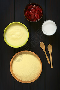 甜点木质碗中原生血素的涂片配有Semolina布丁牛奶杯和一碗草莓甘油用天然光照在黑木上稀饭高架图片