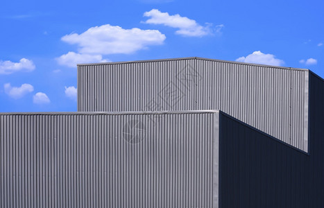 黑色的几何用蓝天空背景的白云对灰色交带金属工厂建筑进行低角观测以察蓝天背景中的白云蓝色图片