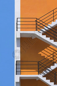 市中心办公室垂直框中橙色和蓝建筑墙外的防火逃逸处表面的阳光和阴影栏杆背景图片