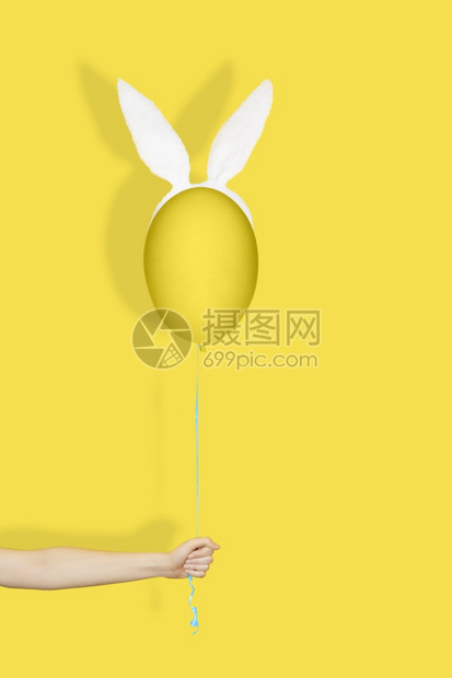垂直的庆典细绳手在兔子耳朵里拿着一个黄蛋像气球一样的黄色鸡蛋在弦上单色东方人创意最小概念Hand在兔子耳朵里拿着黄蛋就像气球在绳图片