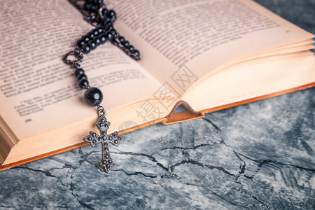 天主教奉献圣经上的黑玫瑰和十字在灰色桌上的学校里宗教祷告图片