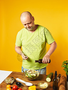 吃餐桌上新鲜沙拉成分中年男子倒油黄色背景老化饮食图片