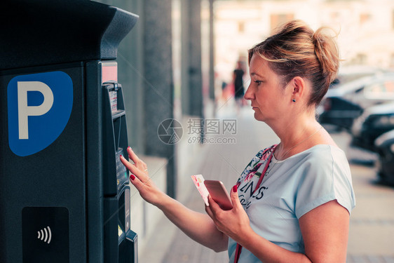 妇女用借记卡或手机购买停车罚单站在机旁边和使用借记卡或移动电话购买停车罚单的妇女車處电子的城市图片