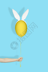 蓝色的传统手在兔子耳朵里拿着一个黄蛋像气球在轻蓝背景的绳子上像气球创以东方最低概念汉在兔子耳朵里拿着一个黄色鸡蛋如浅蓝背景的气球图片