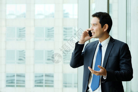 商人通过窗户城市观视办公室建筑内部背景商人电话交谈智能商业人讲智能电话领导者专业的称呼图片