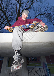 坐在一个掩体的混凝土层上一个手拿着滑板的不快乐长相青年街头生活绞刑滑板手图片