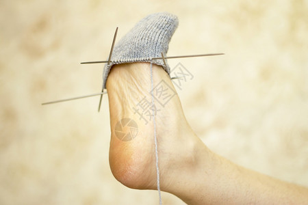 短袜工作女人在轻光背景下她的腿上试一只未完成的灰色羊毛袜纤维图片