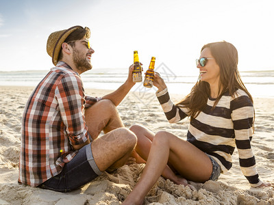 在海滩上玩乐笑和喝啤酒的年轻夫妇闲暇乐趣日落图片