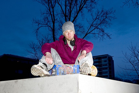 阴沉生活风格的肖像一个不快乐的年轻长相手拿着滑板的年轻人坐在一个掩体的混凝土墙壁上出去黄昏图片