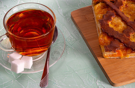 糕点木制的营养丰富一杯加柠檬派的烈茶和切餐板上的馅饼图片