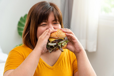 一顿饭饥饿超重的年轻亚洲女人拿着汉堡包她饿了所有的时间和过量吃饱谷食和狂她的生活方式正在吃快餐所有时间不健康的概念饥饿暴饮食背景图片