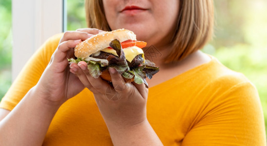 潮人美国女饥饿超重的年轻亚洲女人拿着汉堡包她饿了所有的时间和过量吃饱谷食和狂她的生活方式正在吃快餐所有时间不健康的概念背景图片