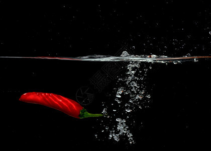 流动的可口进入红辣椒在黑色背景下与气泡一起坠入水中图片