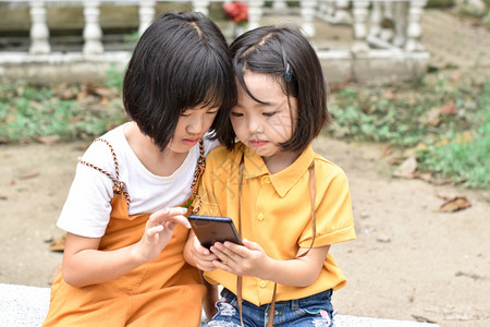 姐两个妹子女在户外公园玩智能手机游戏和幸福坐着图片