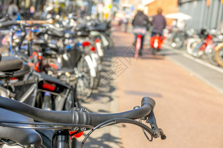 荷兰在阿姆斯特丹的自行车泊停放日荷兰阳光在Bike泊车场和一对夫妇骑自行车者与两辆赛手一起离开关注焦点的SunnyDay停車處健图片
