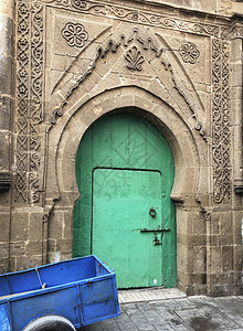 非洲街道建筑物一个亮绿色的大门与摩洛哥Essaouira苏克建筑的蓝色手推车和古老石墙形成对比图片