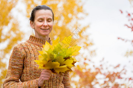 愉快一个笑着的成年天主教女人秋在公园里采黄色的树叶美丽季节图片