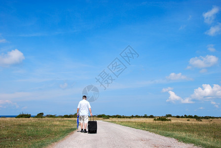 美丽自然晴天在阳光明媚的风景中旅行者带着手提箱走在乡村公路上图片