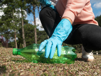 户外自然环境的身戴手套近亲志愿者从公园草地上捡起一个塑料瓶子以保护环境和阻止塑料污染的概念组织在公园中从草地上捡起一个塑料瓶图片