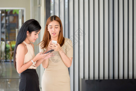 细胞两位现代年轻美丽的亚洲女在智能手机上打字留言办公室女士图片