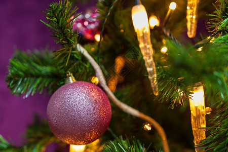玩具绿色紧贴的圣诞树装饰在紫色主题中前景和蜡烛灯背上有一个突出的紫色球石榴图片