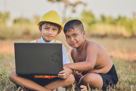 安全帽童年电脑快乐的男孩子在户外使用计算机制造硬帽背景