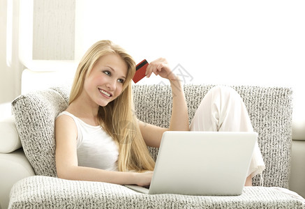 技术红色的在线购物美丽的金发女坐在索法的沙发上仅有图片