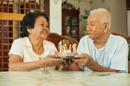 活的妻子亚洲人高龄夫妇在客厅里拿着蛋糕笑图片