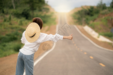 冒险搭便车者年轻的路上搭便车妇女空农村曲线沥青路后视图片