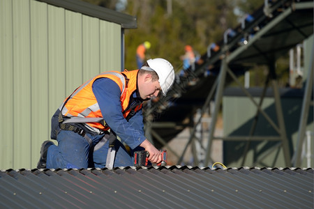 标记一名建筑工身着安全带在标有拆除志的建筑物上从事高无机组工人作的屋顶铁可见度建设者图片