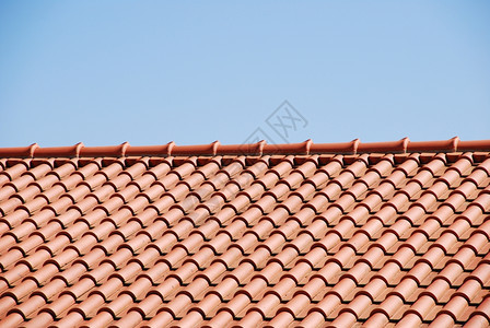 排在蓝天背景下房子屋顶上的橙色瓷砖盾图片