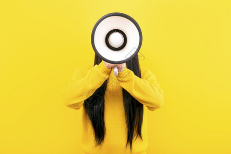 声音穿着黄色毛衣的女孩用黄背景的扩音器沟通大喊叫图片