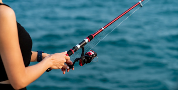 爱好妇女手持有海背景的渔棍在日落时捕鱼钩钓运动图片