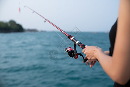 妇女手持有海背景的渔棍在日落时捕鱼海洋娱乐电缆图片
