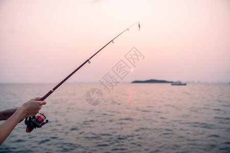 钩景观妇女手持有海背景的渔棍在日落时捕鱼爱好图片