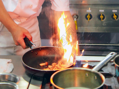 可口油炸厨师在房炉灶的煎锅中用火焰做饭炉图片