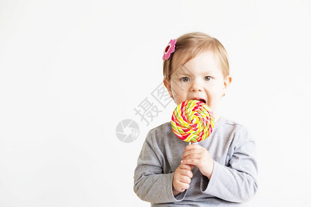 喜悦俏皮小女孩吃棒糖快乐的孩子与大美味糖果画上小女婴的肖像在白色背景下好的图片