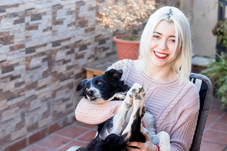 笑玩金发的年轻女人在露天坐阳台上拥抱她的狗微笑图片