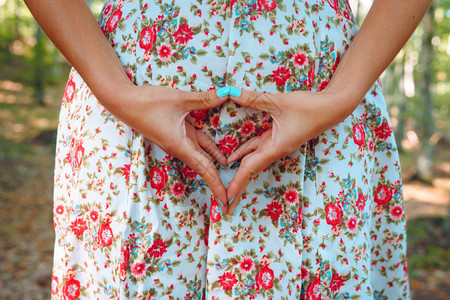 手臂年轻的清洁身着白夏洋装和鲜花印刷品的年轻女中产体用触摸下腹部生殖器区域的手指和拇将双三角形指和拇握在一起图片