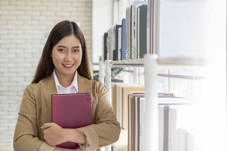 女生手握书本在书架旁微笑图片